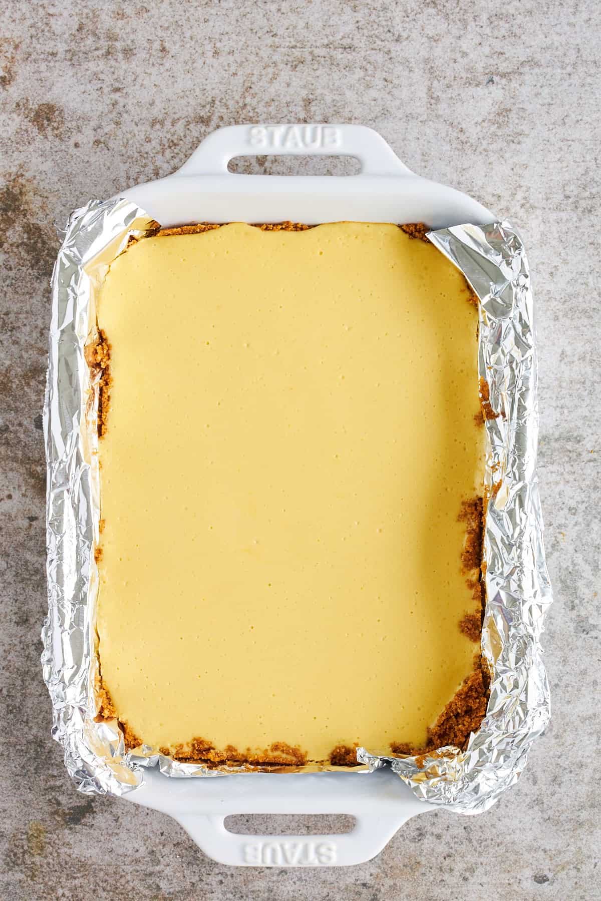 A key lime filling spread over a graham cracker crust in a baking dish.