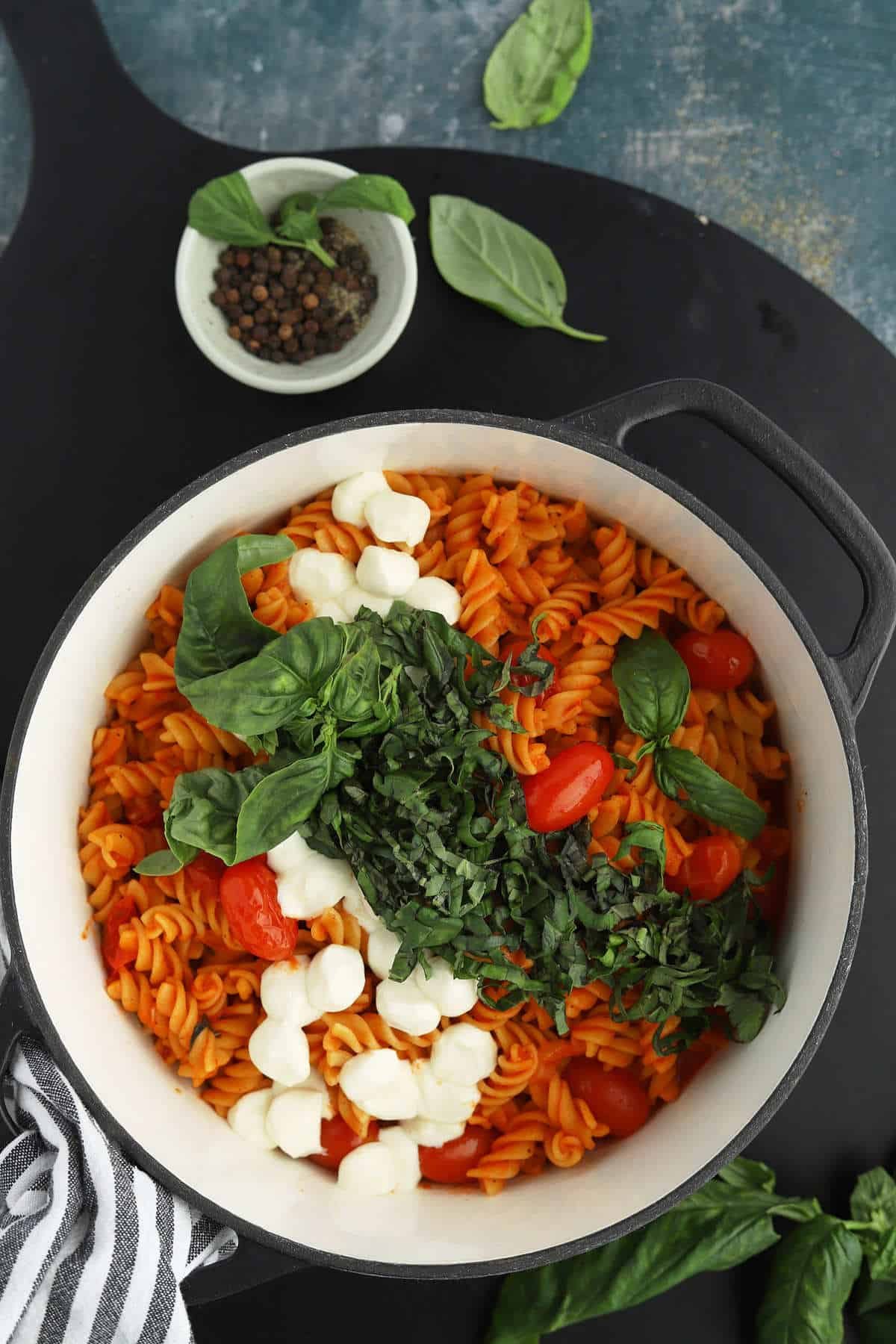 overhead image of caprese pasta in a white pot with tomatoes, basil, and mozzarella