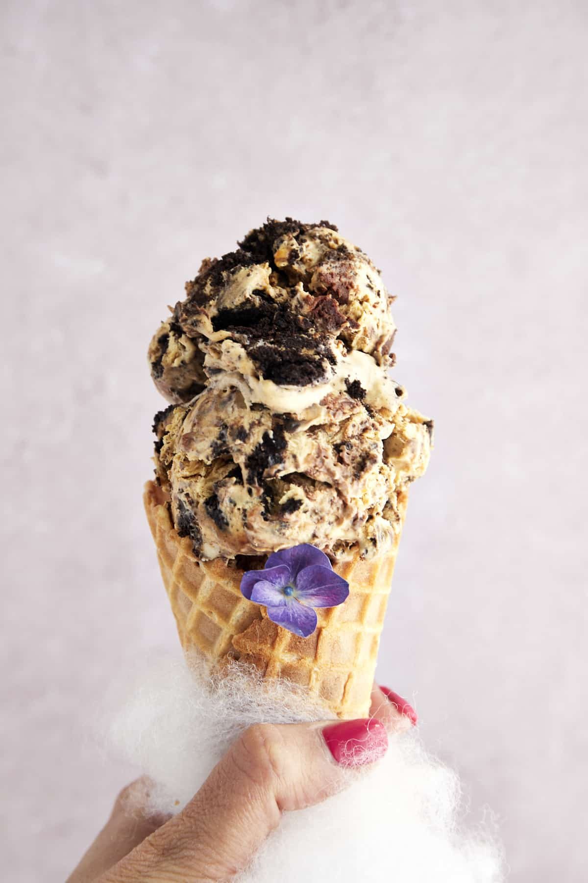 A hand holding a waffle cone with two scoops of mocha Oreo no churn ice cream.