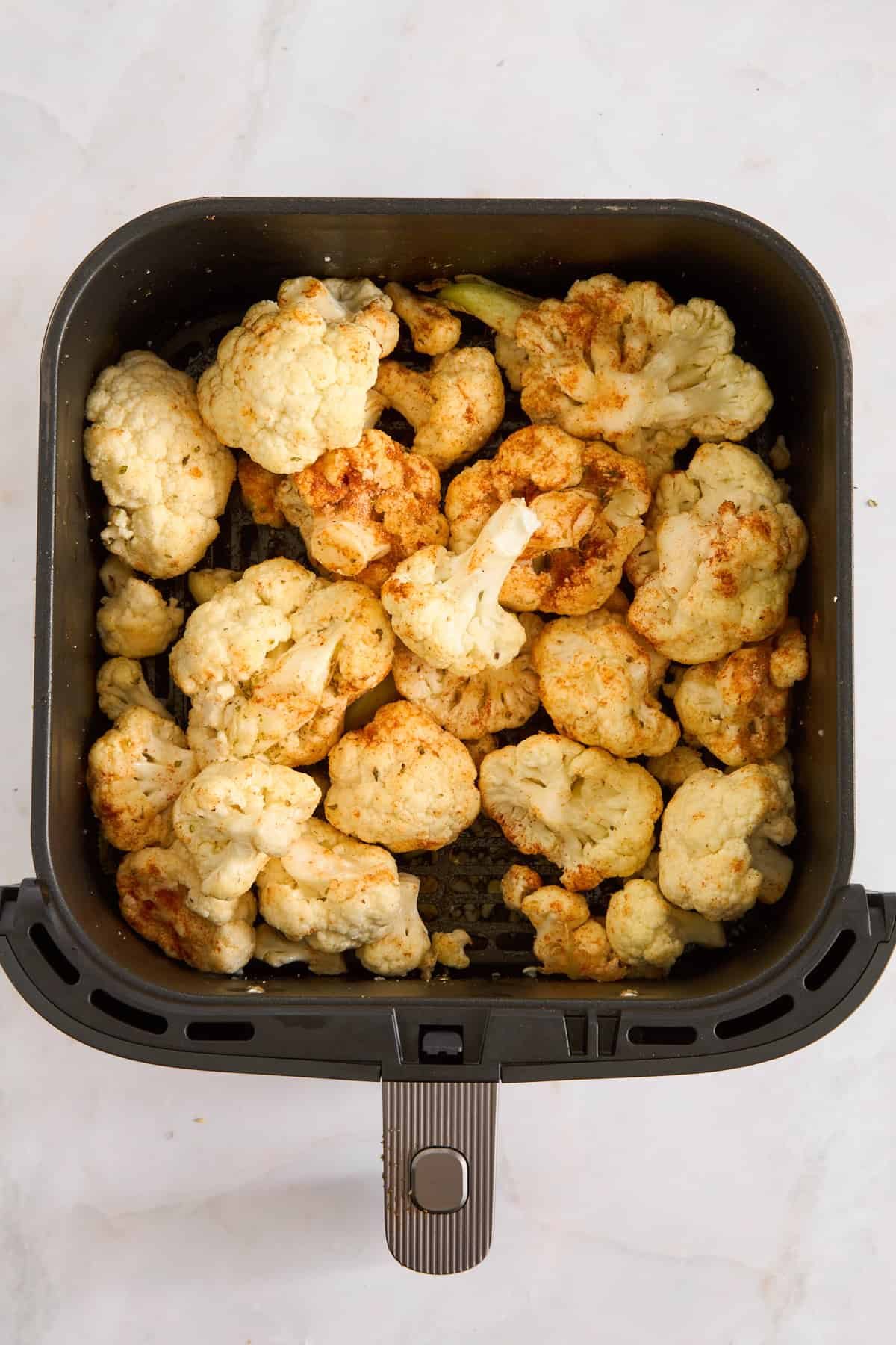 Raw seasoned cauliflower florets in an air fryer basket.