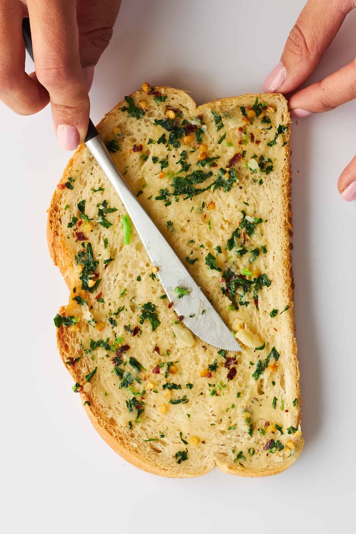 Herbed butter being spread over a slice of bread.