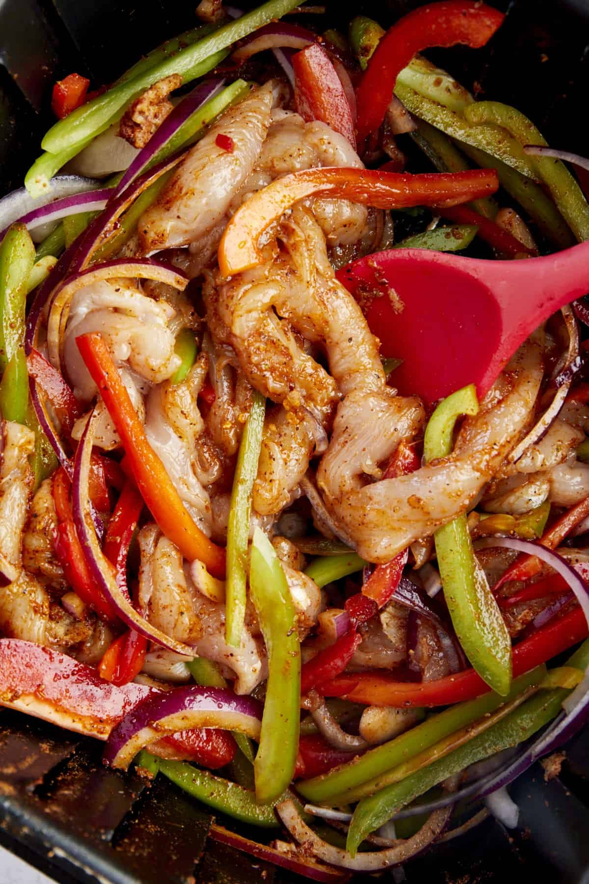 Raw chicken, peppers, and red onions coated with taco seasoning in an air fryer.