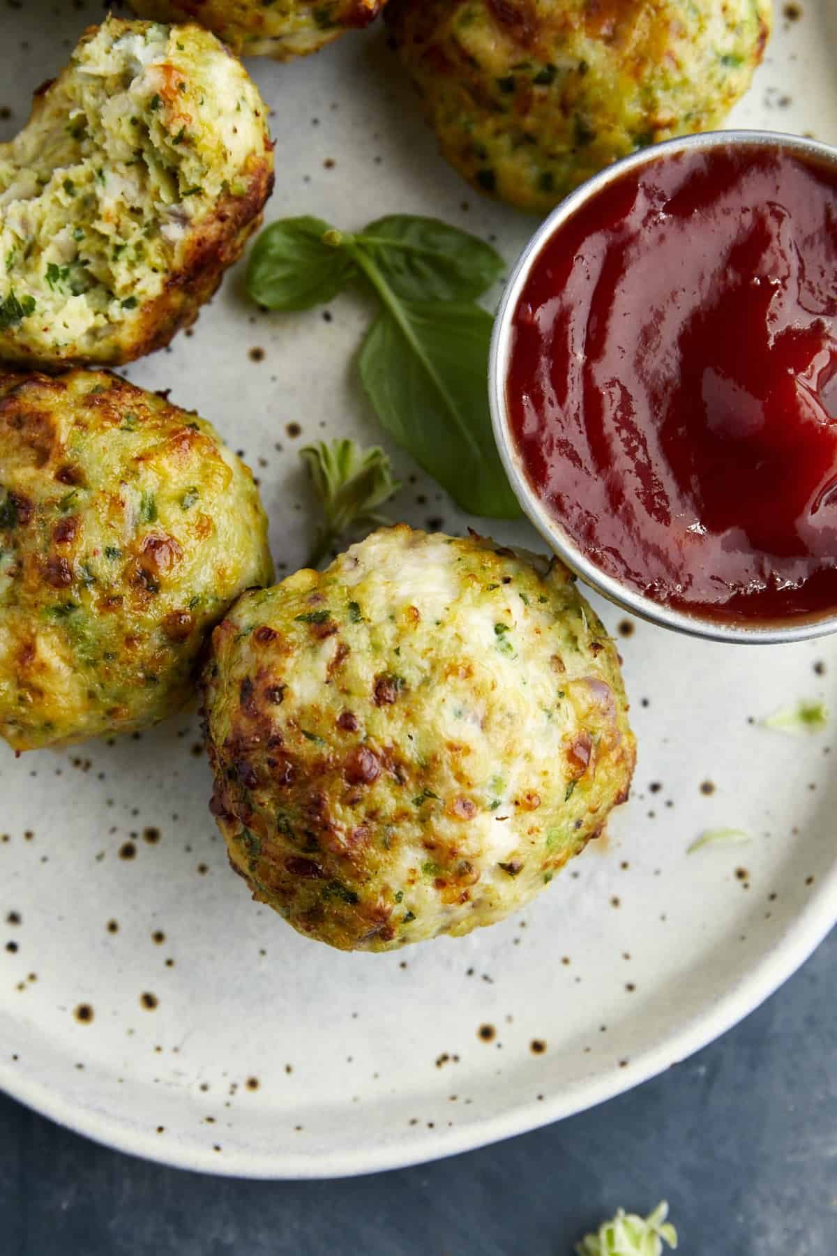 Close up of a plate of Air Fryer Jalapeño Cheddar Chicken Meatballs with a bowl of ketchup on the side and a bite missing from one.