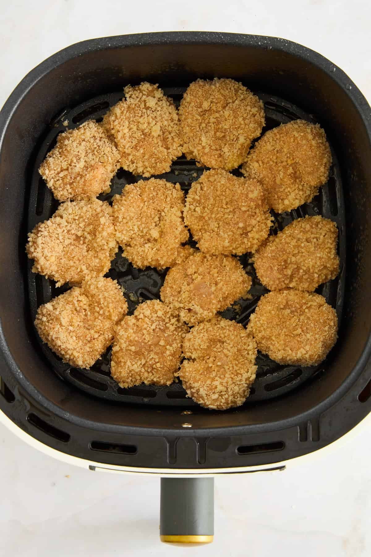 Raw chicken nuggets in an air fryer basket.