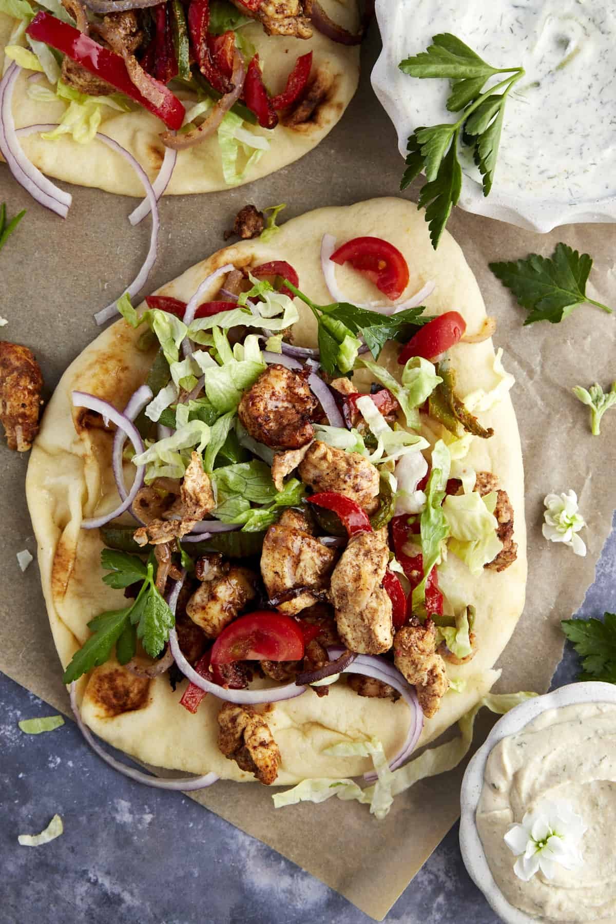 An air fryer chicken shawarma wrap with naan bread, lettuce, tomatoes, and red onion with a shite sauce on the side.