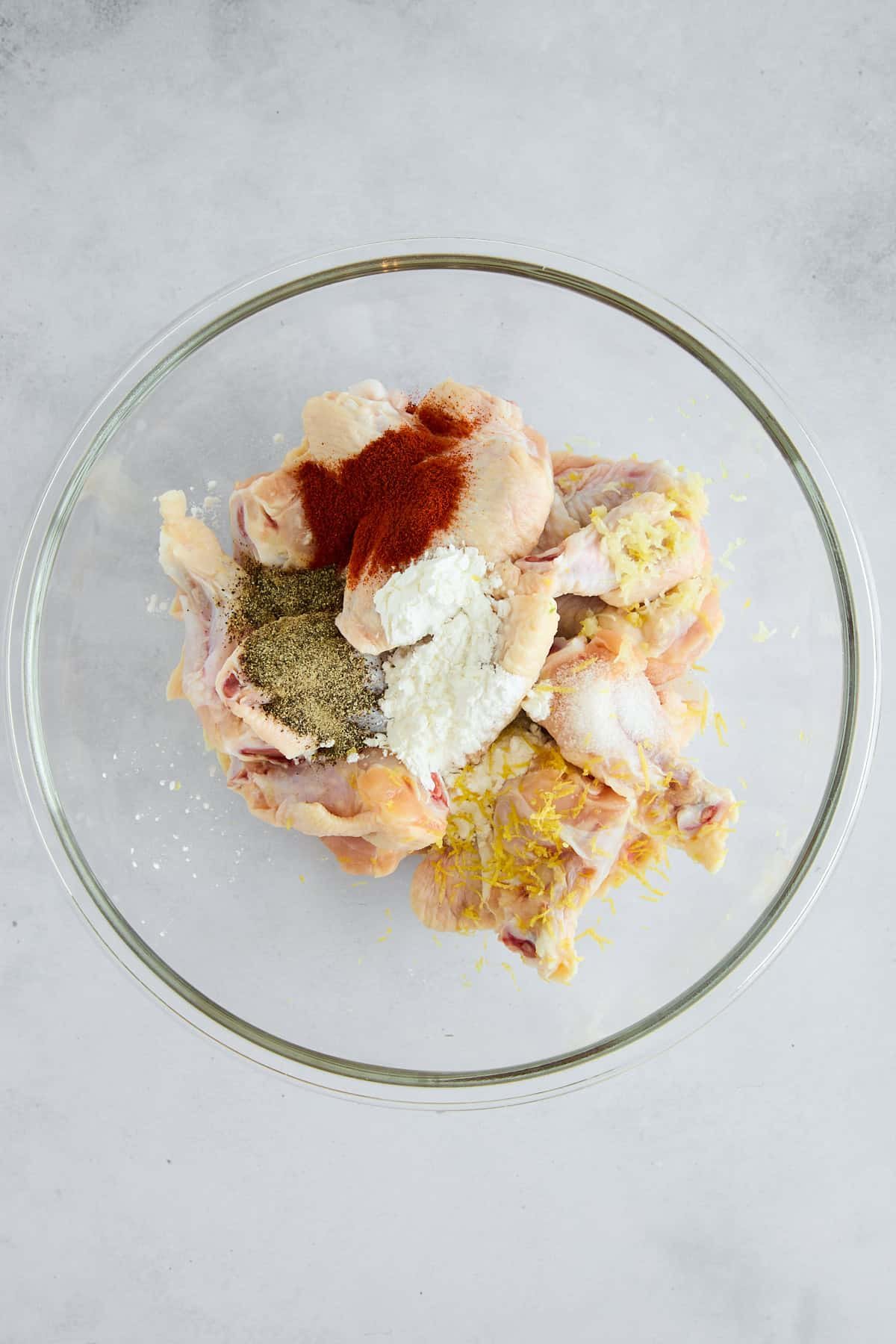 Raw chicken wings in a bowl topped with seasonings.