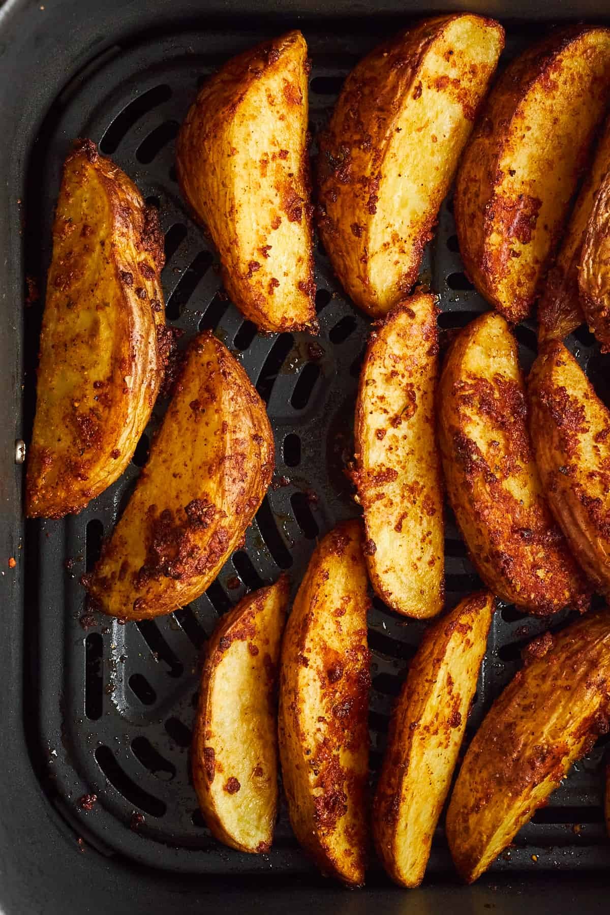 Cooked garlic parmesan potato wedges in an air fryer basket.