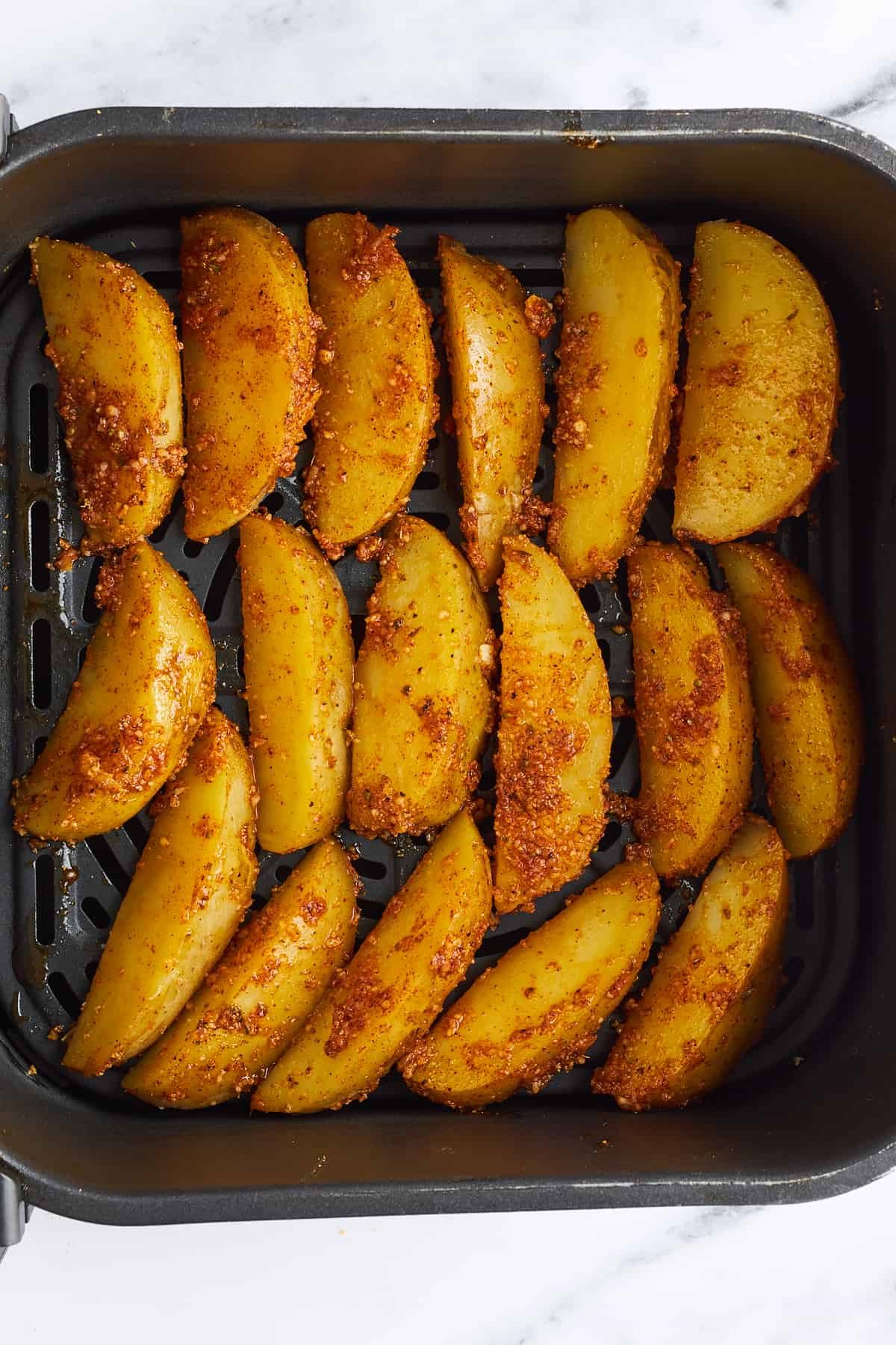 Seasoned unbaked garlic parmesan potato wedges in an air fryer basket.