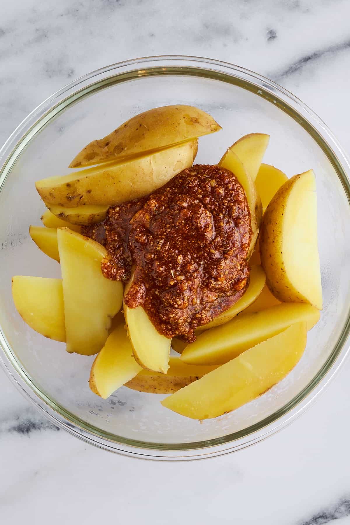 Potato wedges in a bowl with a seasoning rub on top.