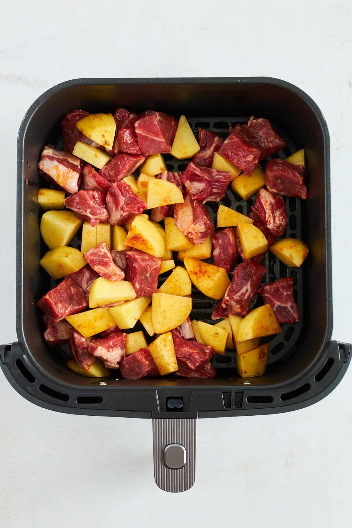 Raw steak and potatoes in an air fryer.