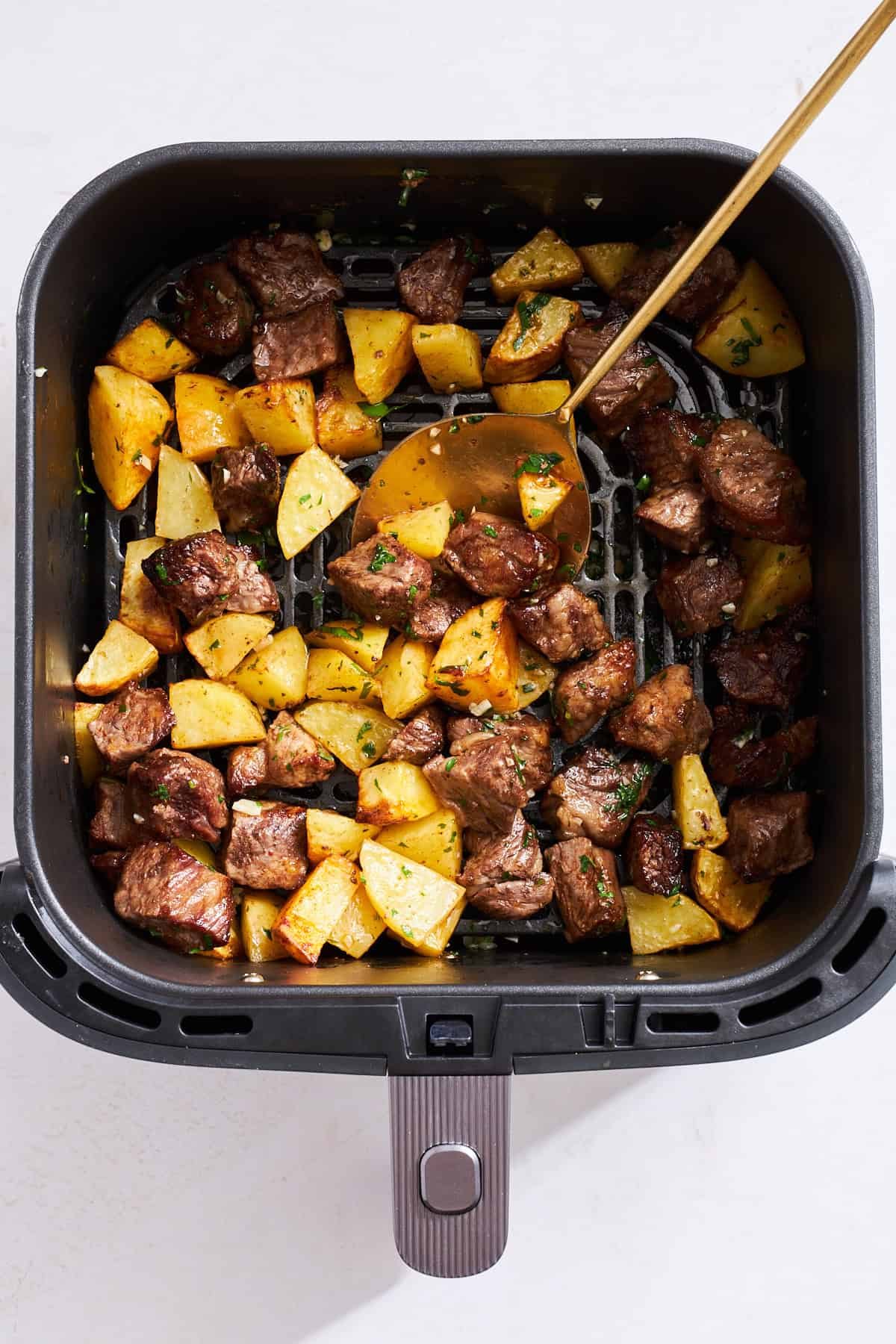 Cooked steak and potato pieces tossed with a garlic butter sauce in an air fryer.