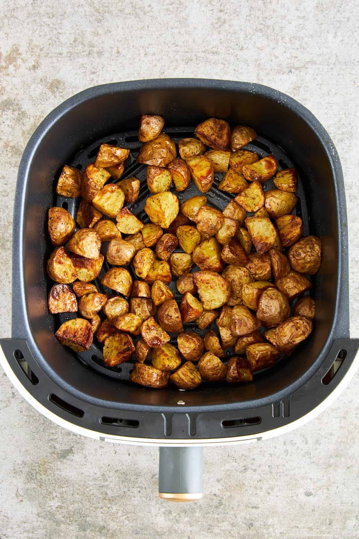 Cooked Greek potatoes in an air fryer basket.