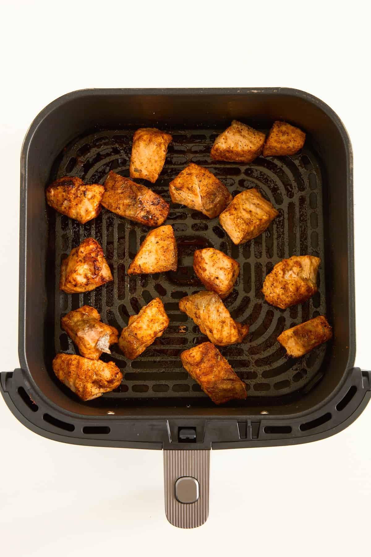 Cooked salmon bites in an air fryer basket.