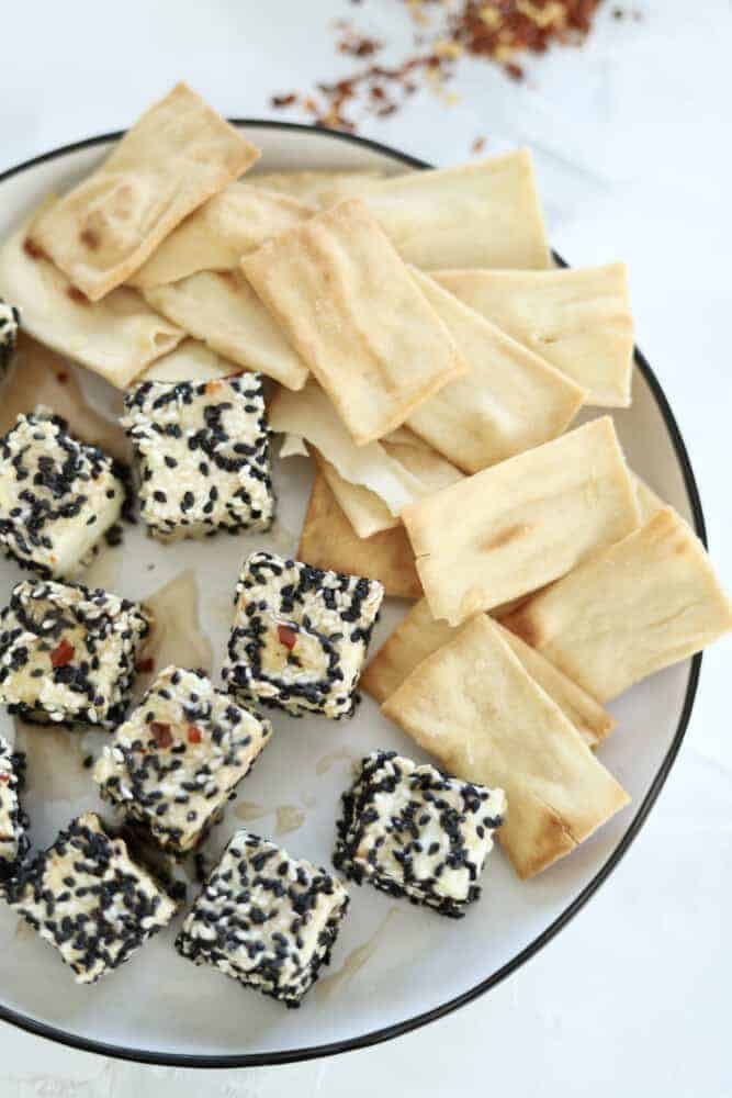 a plate of sesame crusted air fryer feta cubes with pita chips on the side