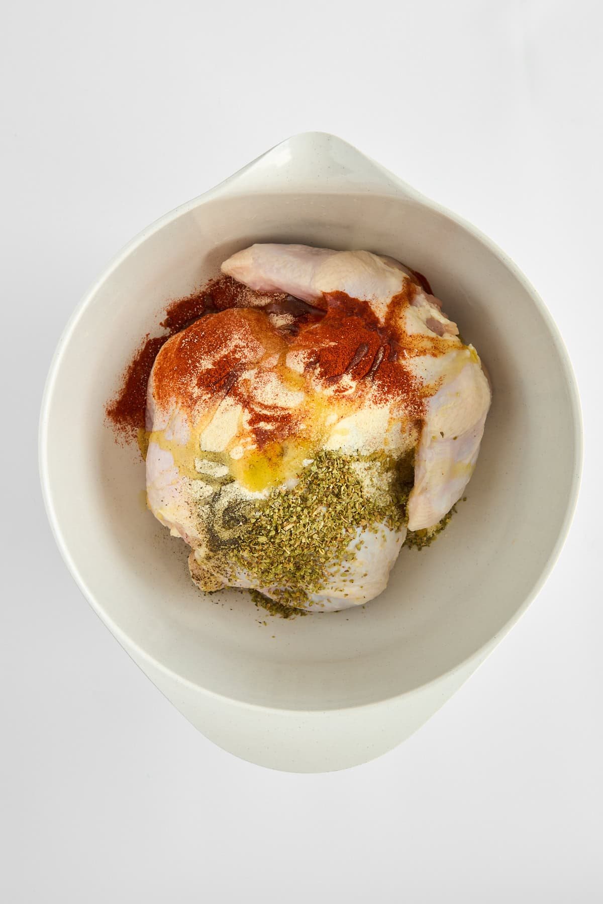 A raw whole chicken covered with seasonings in a bowl.