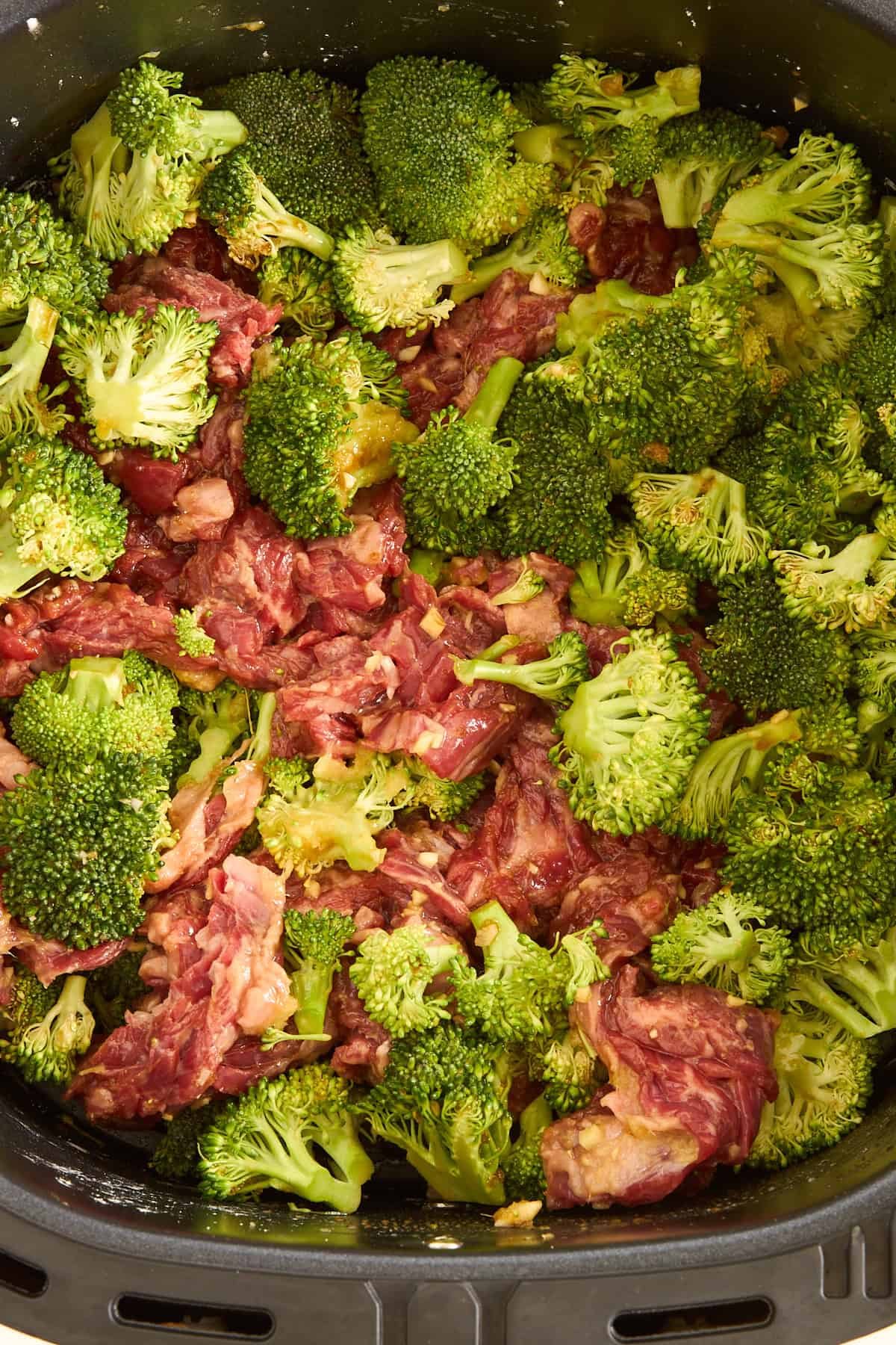 Raw air fryer beef and broccoli in an air fryer basket.