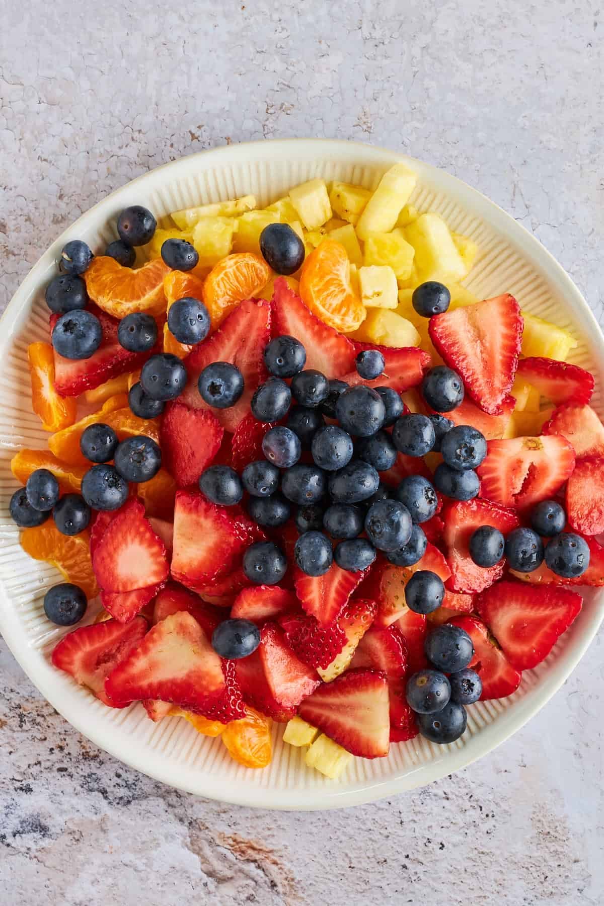 A bowl of strawberries, blueberries, pineapple, and mandarin oranges.