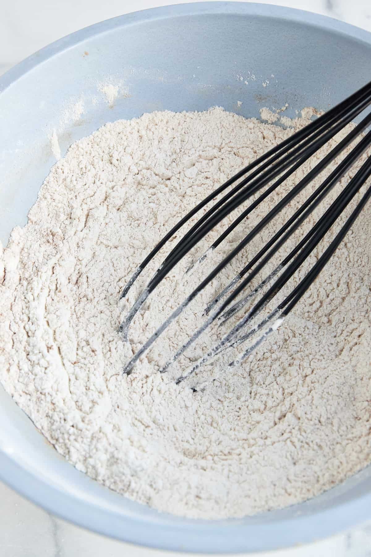 Dry muffin batter ingredients being whisked in a blue bowl.