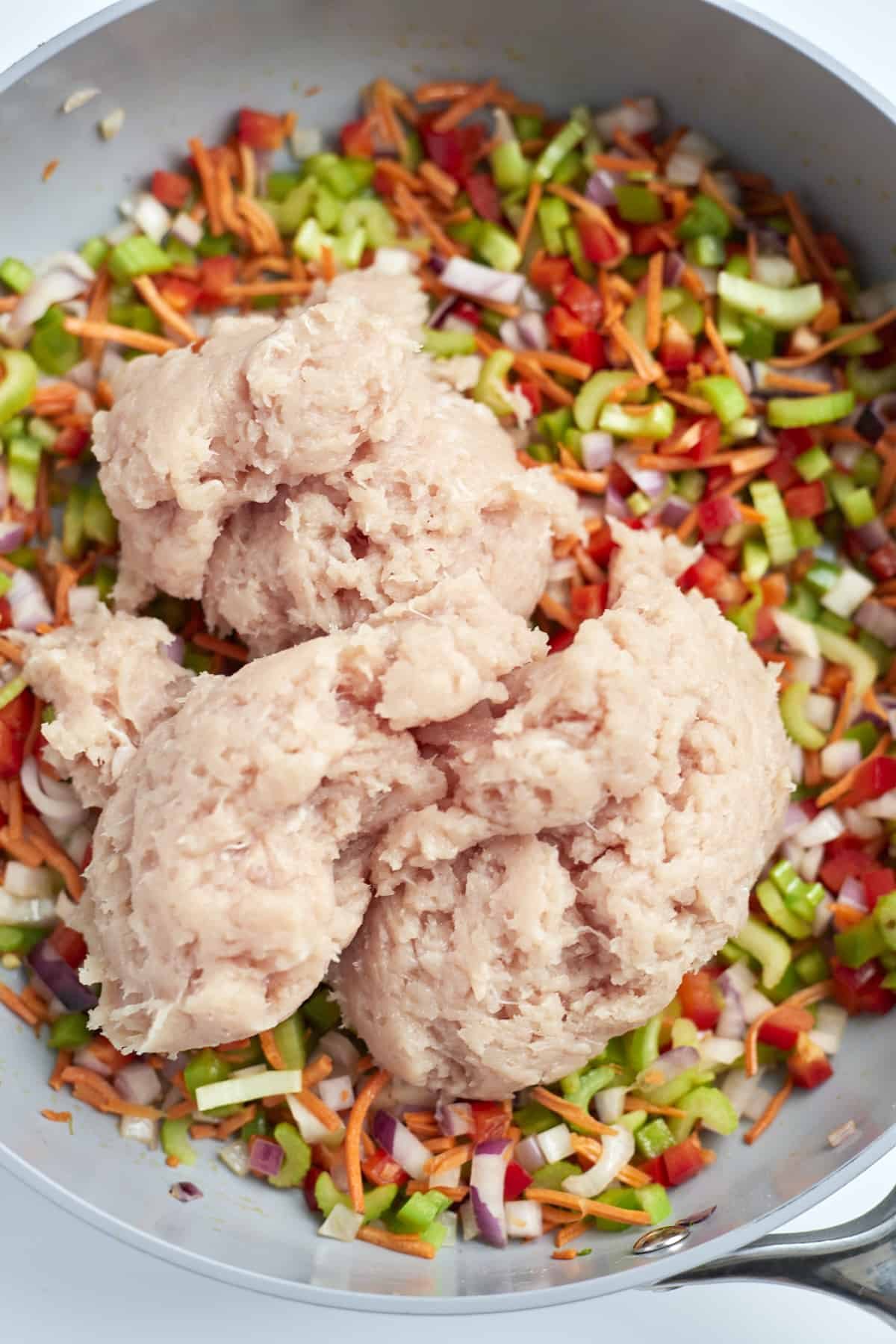 uncooked ground chicken on top of veggies in a skillet.