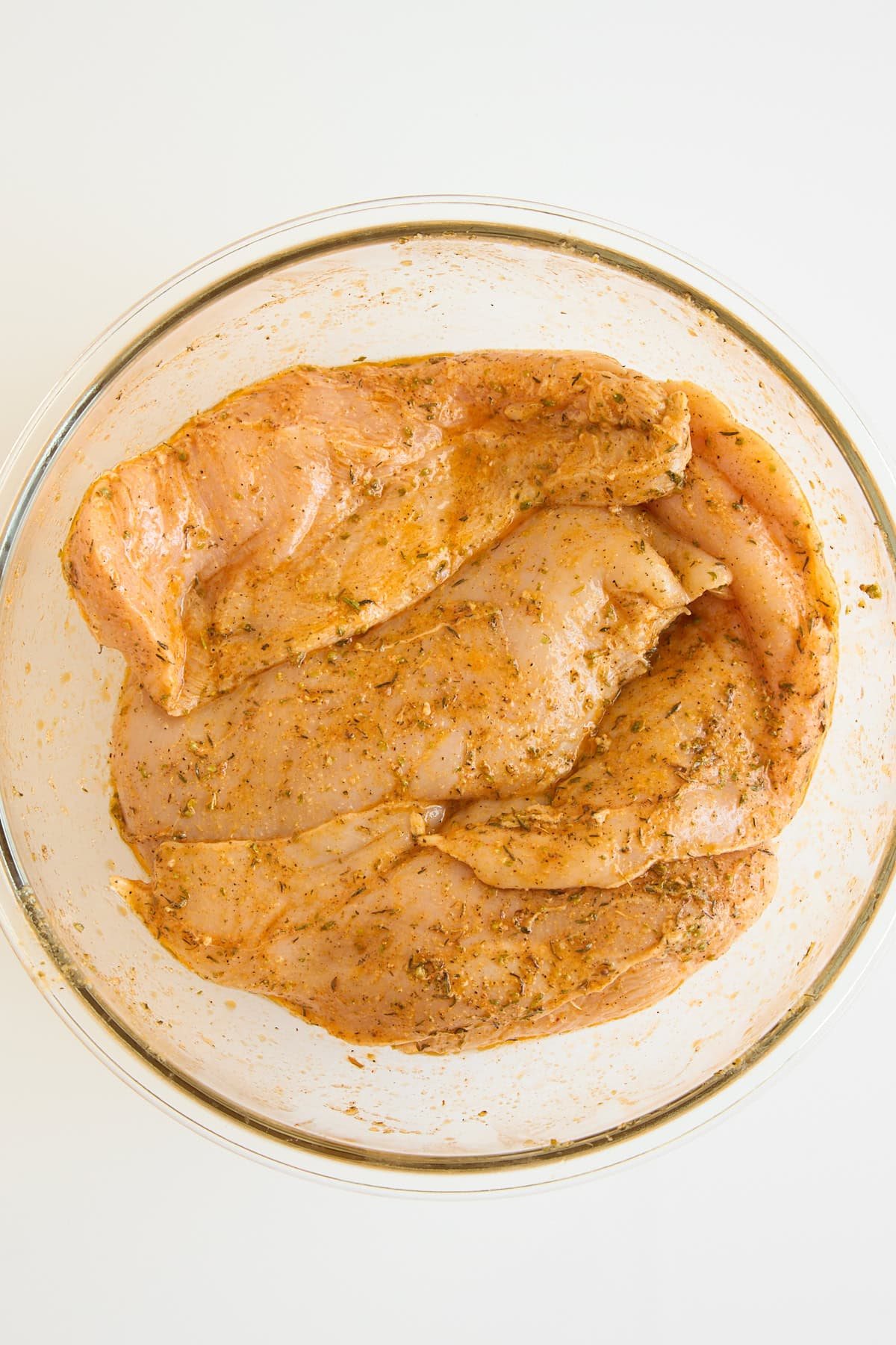 Raw chicken breasts marinating in a bowl.