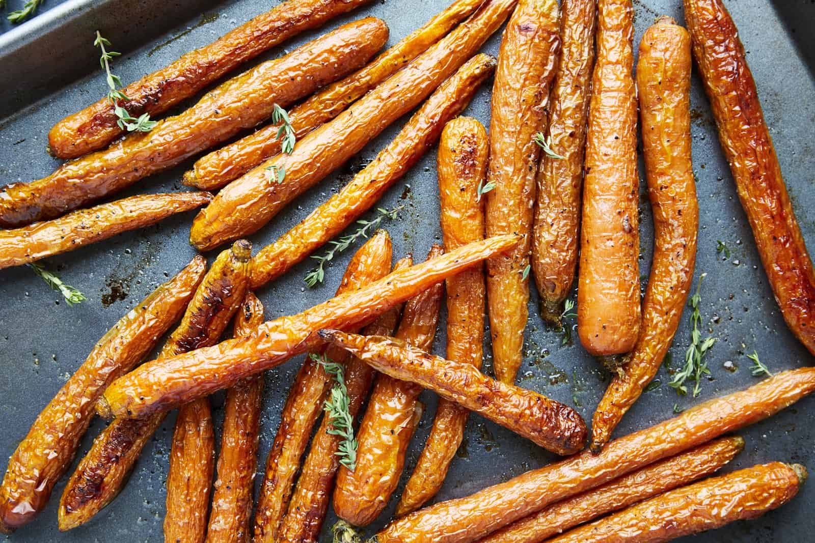 Oven baked carrots topped with fresh herbs on a baking sheet.