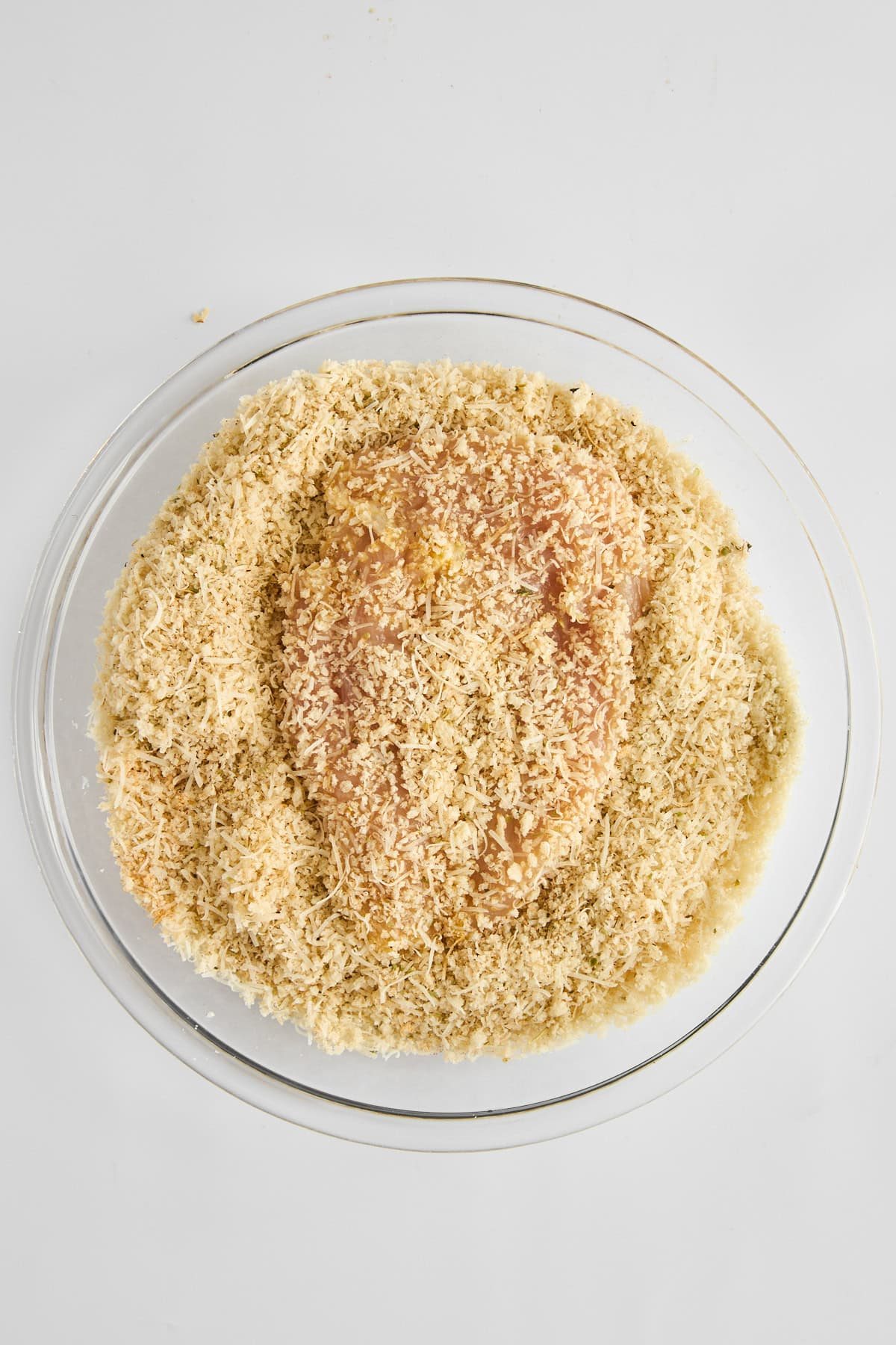 A piece of chicken in a bowl of breading.