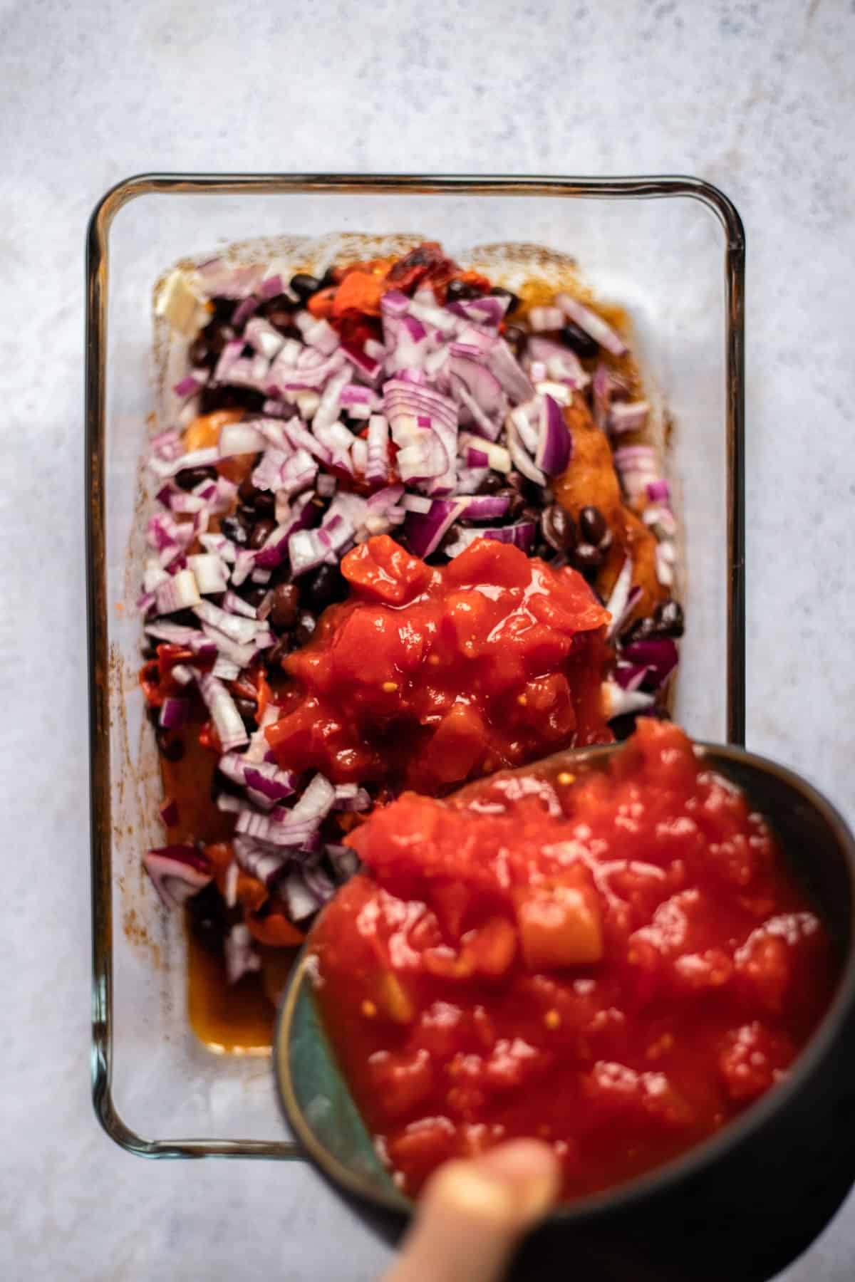 raw seasoned chicken topped with black beans and diced red onions with salsa being poured on top