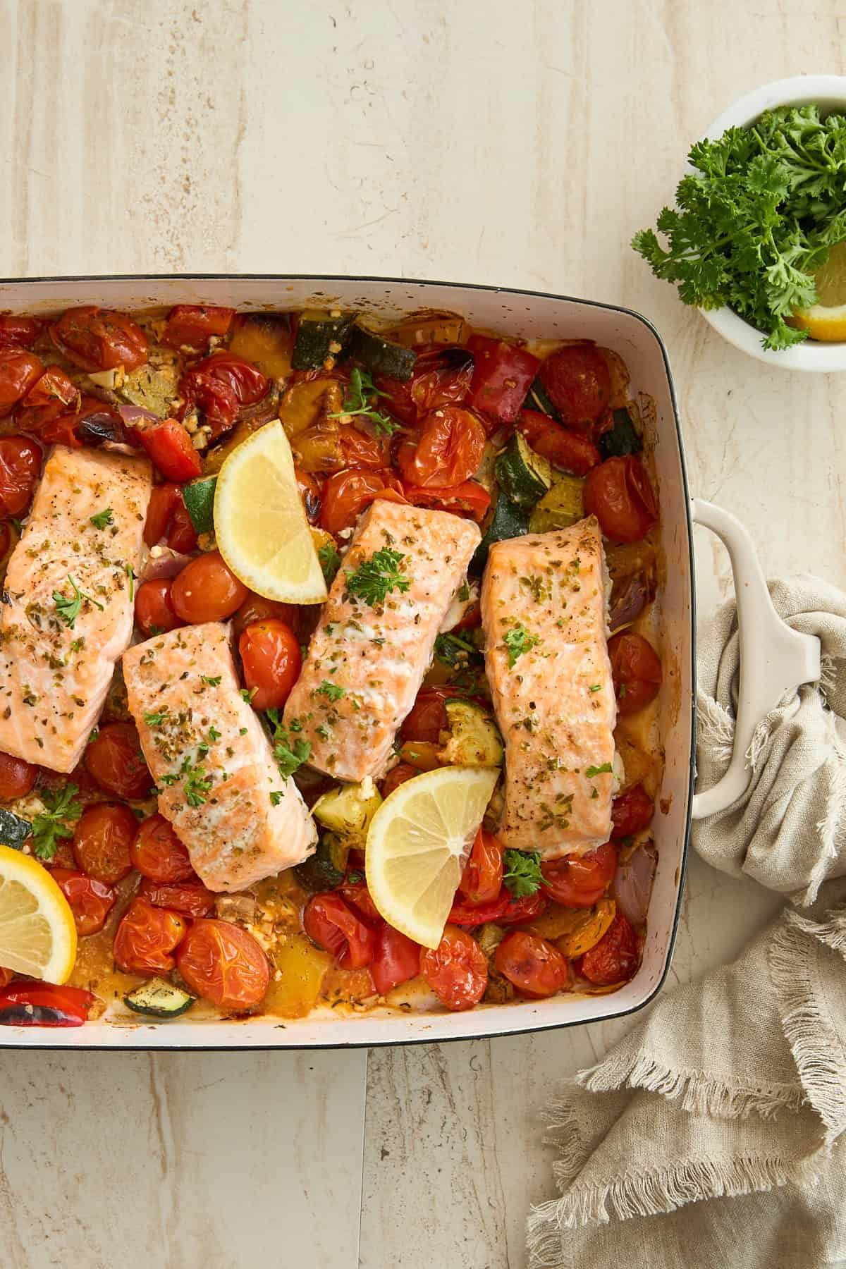 Baked feta salmon in a dish with tomatoes and lemon wedges.