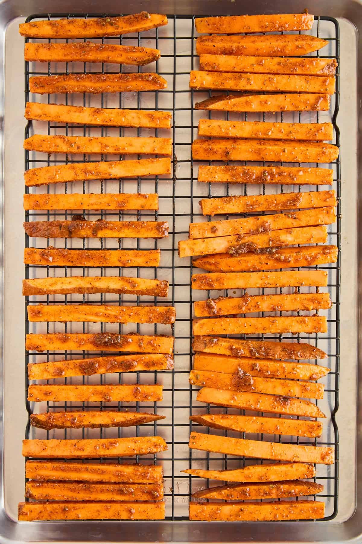 Raw seasoned sweet potato fries on a wire rack on a baking sheet.