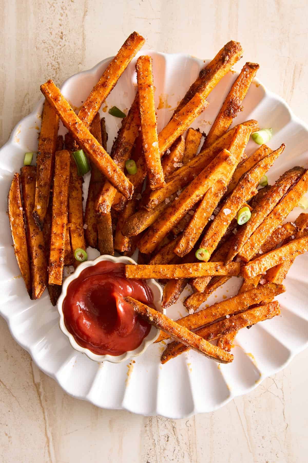 A plate of oven baked sweet potatoes with a side of ketchup.