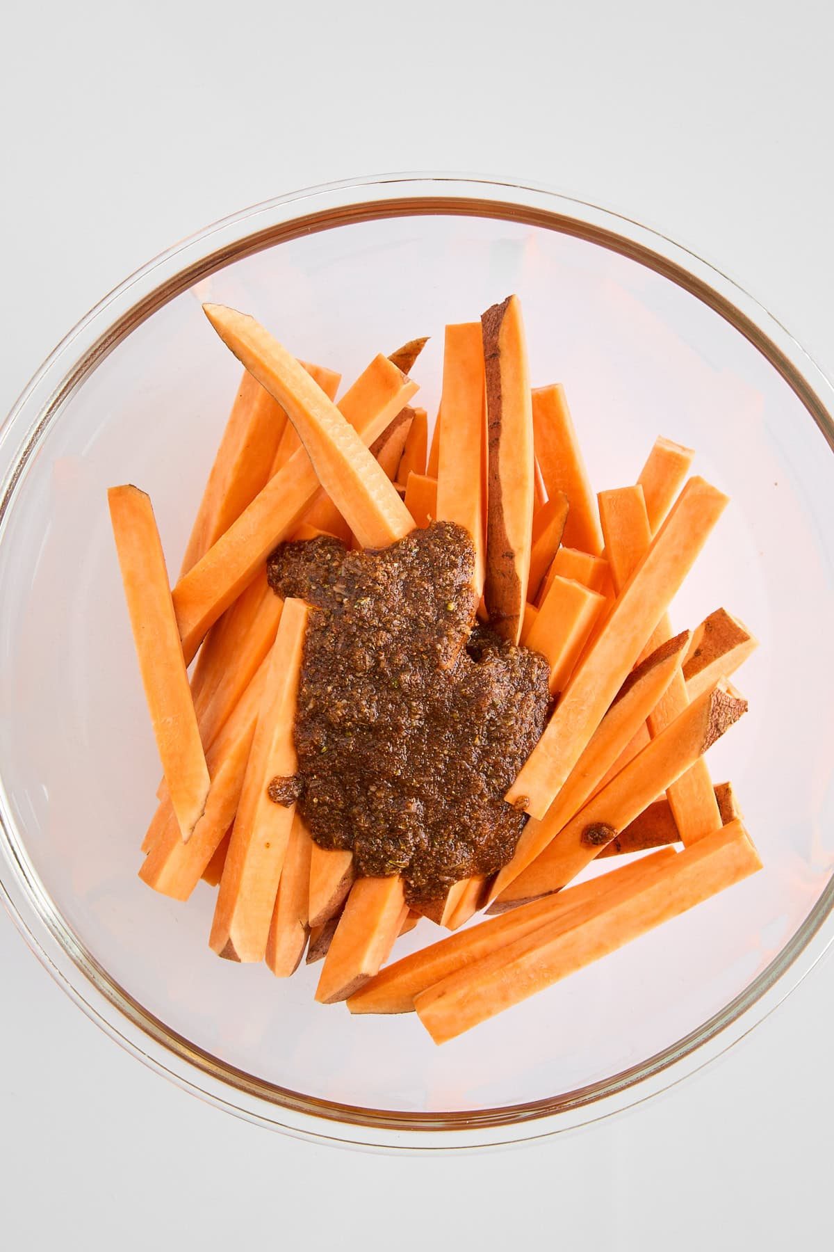 A bowl or raw sweet potato fries topped with a seasoning mix.
