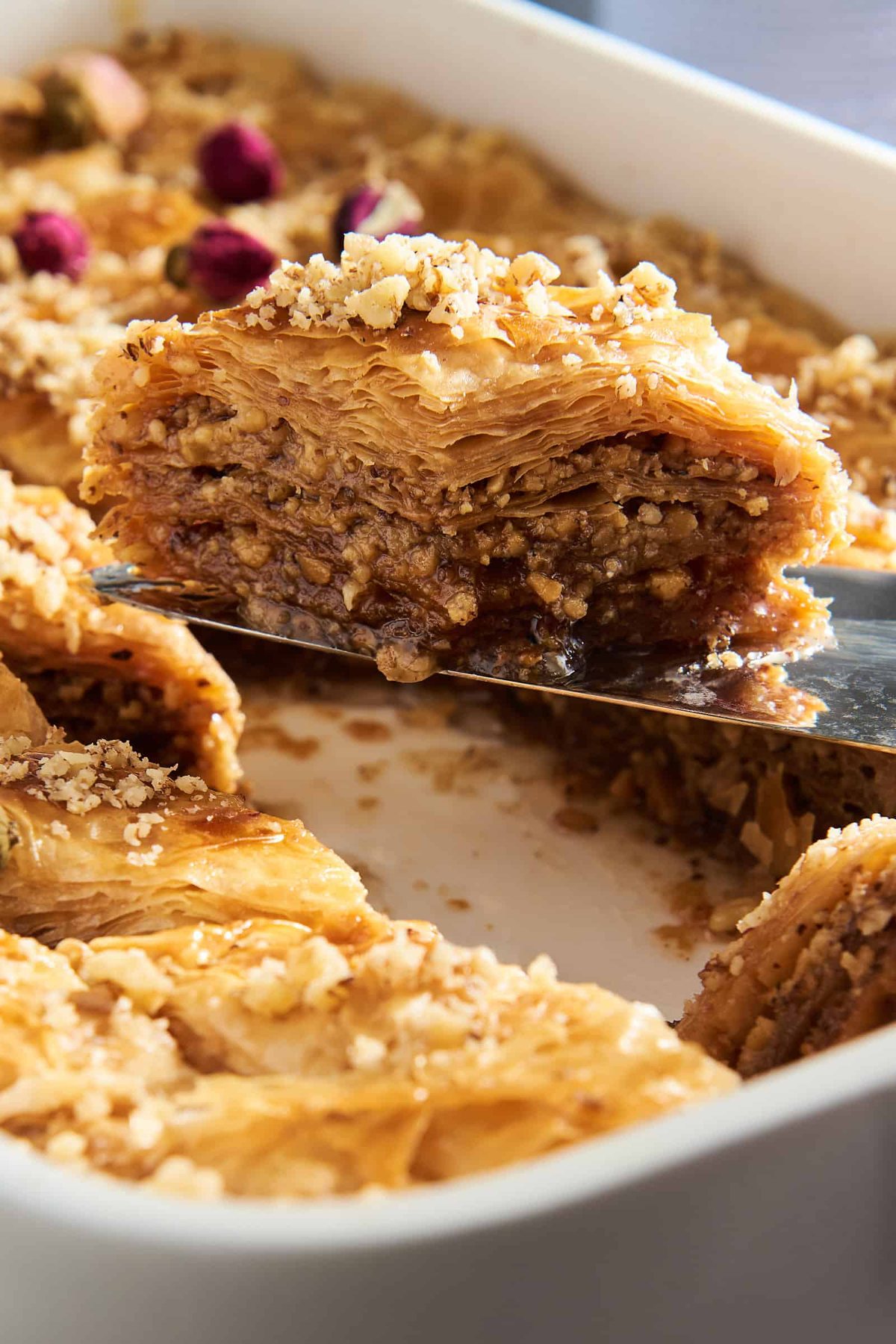 A slice of baklava being lifted from a baking dish full of the dessert.