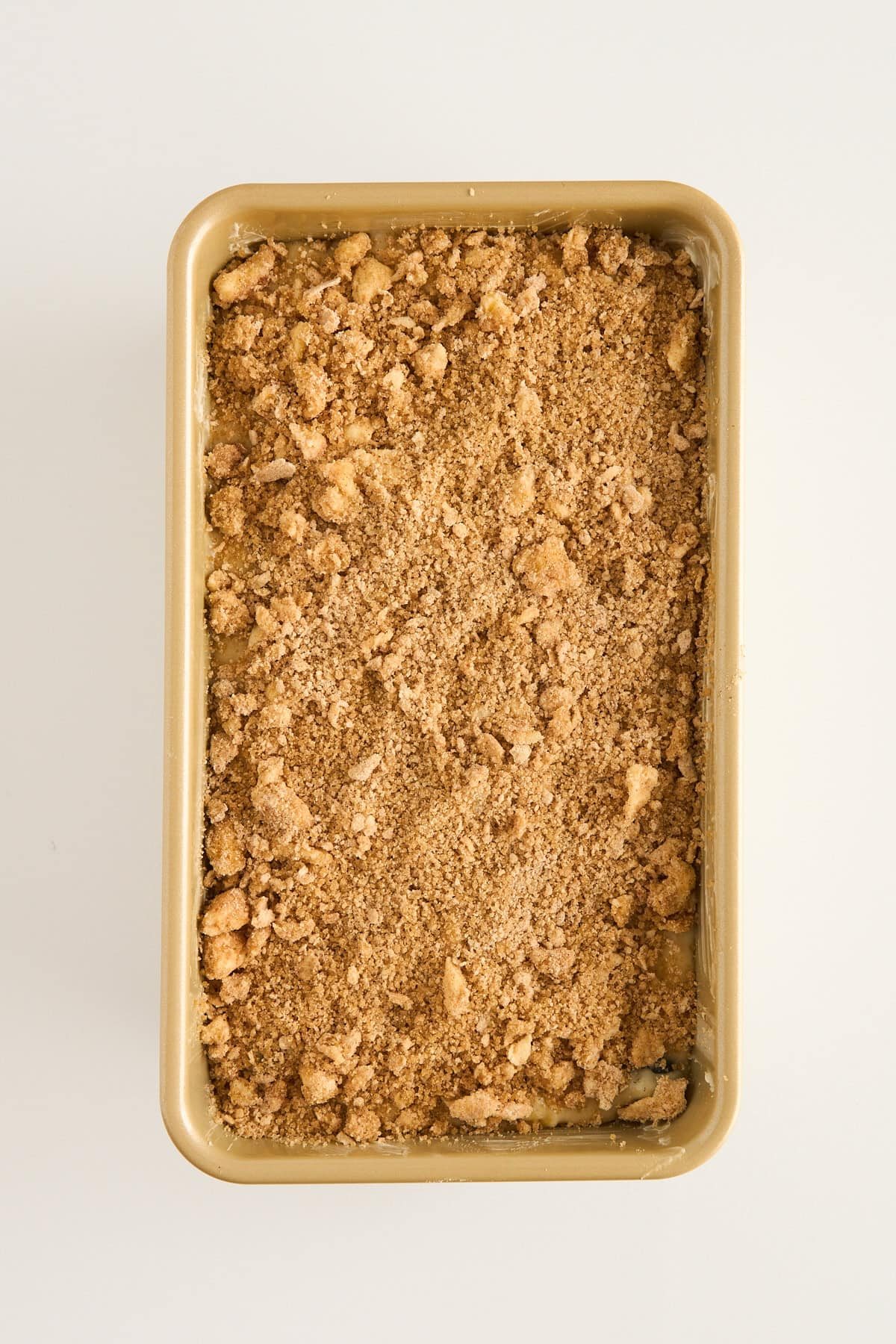 Rectangular baking pan filled with an even layer of crumbly, brown streusel topping on an off-white background.