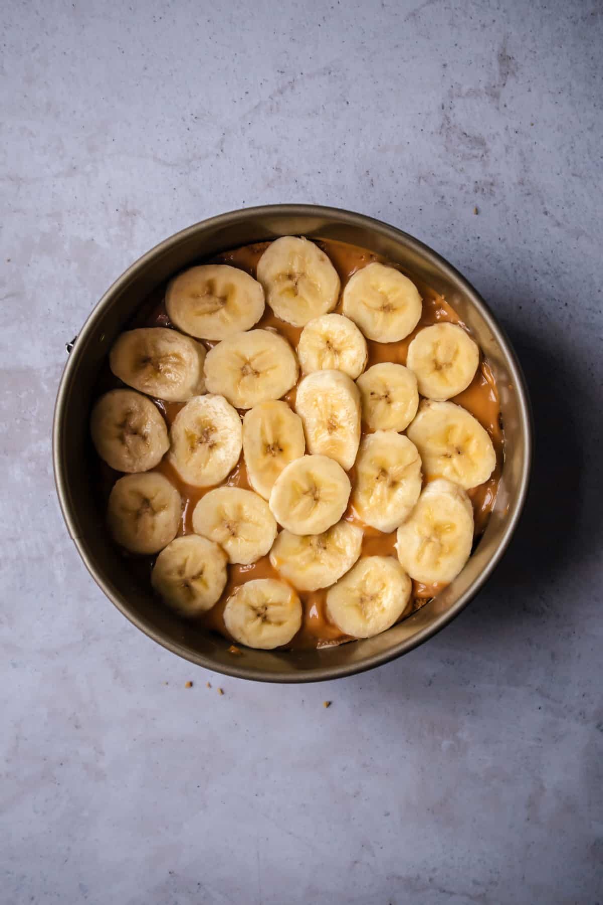 overhead image of a cake pan with a graham cracker crust topped with a layer of dulce de leche and banana slices