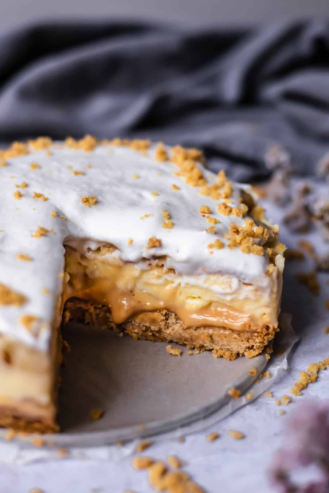 side view of a banoffee pie with a slice cut out showing the layers of crust, dulce de leche, pudding, and cream