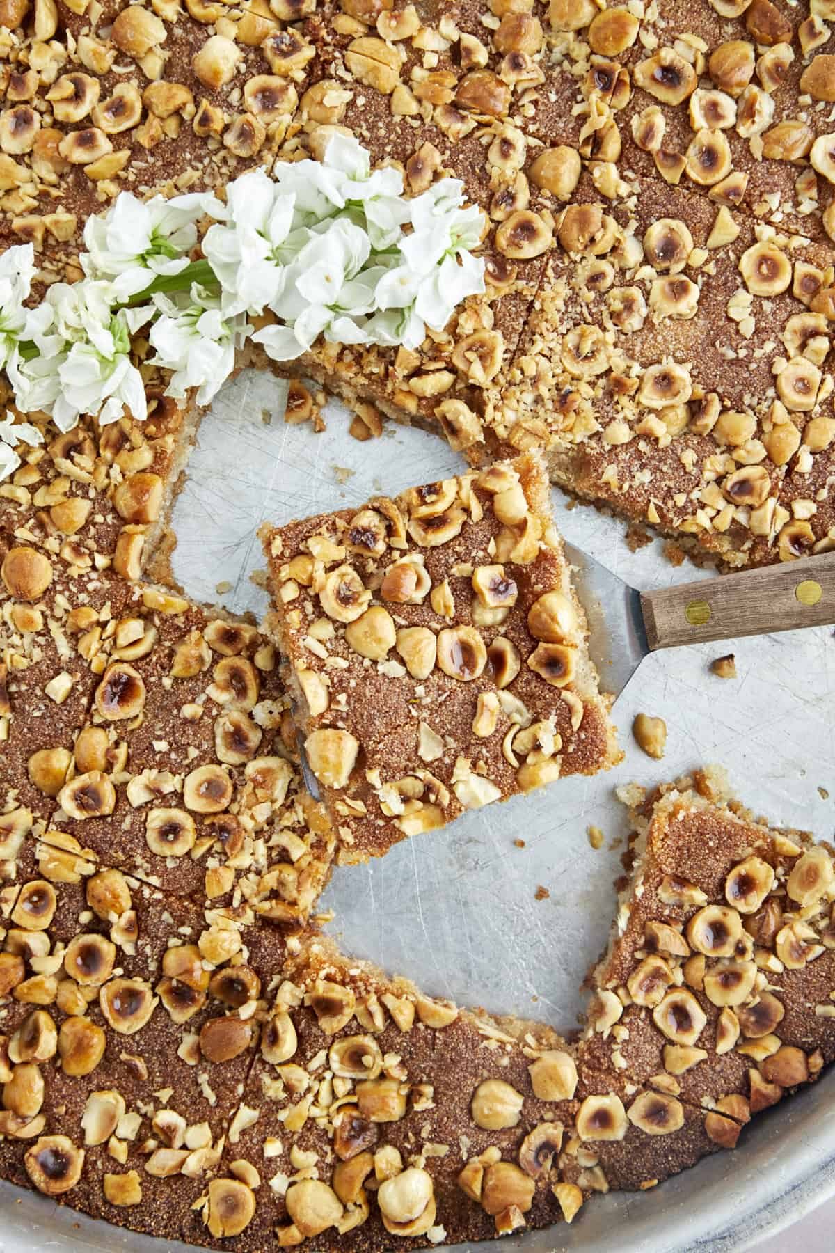 A piece of semolina cake being lifted from a sheet pan.