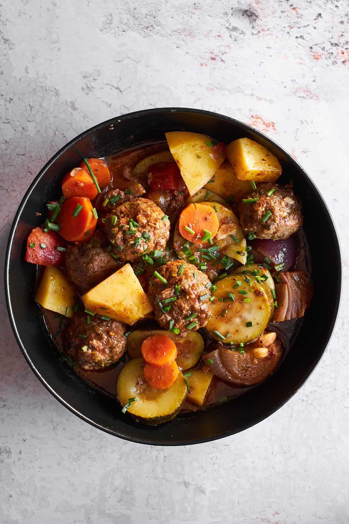 A bowl of beef kofta bake with meatballs and veggies.