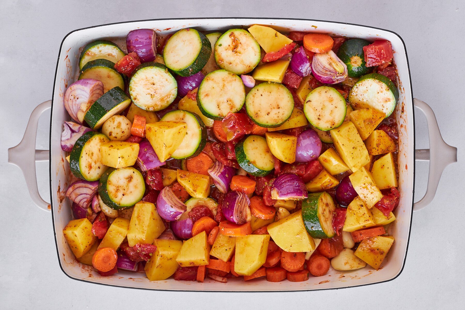 Zucchini, bell peppers, onions, tomatoes, and spices in a baking dish.