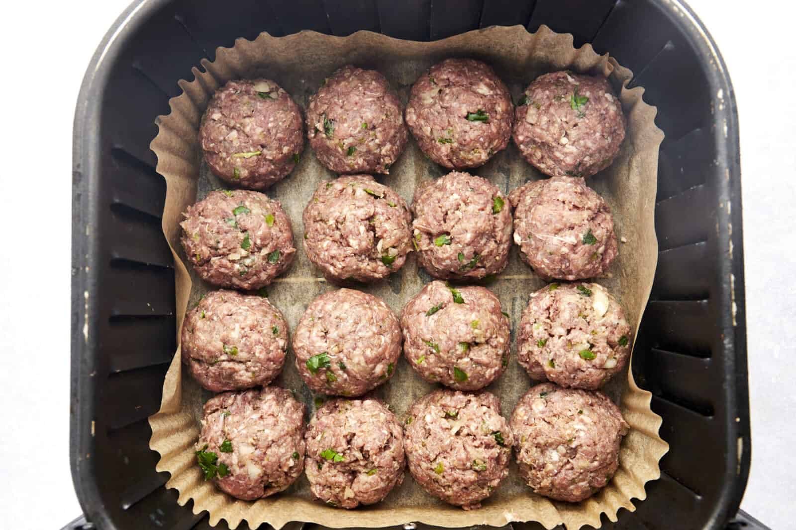 Raw beef kofta meatballs in an air fryer basket.