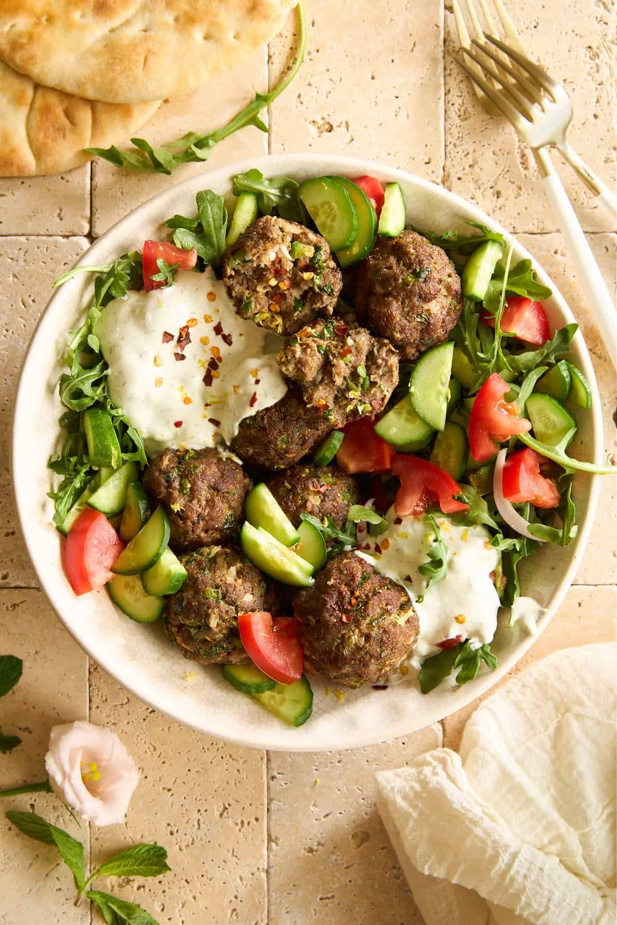 A salad with tomatoes, cucumbers, beef kofta meatballs, and tzatziki.