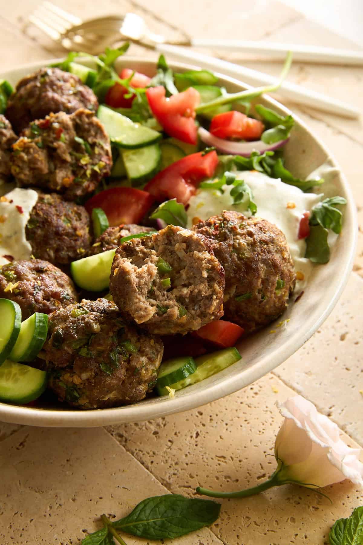 A cucumber and tomato salad with beef kofta meatballs and tzatziki.