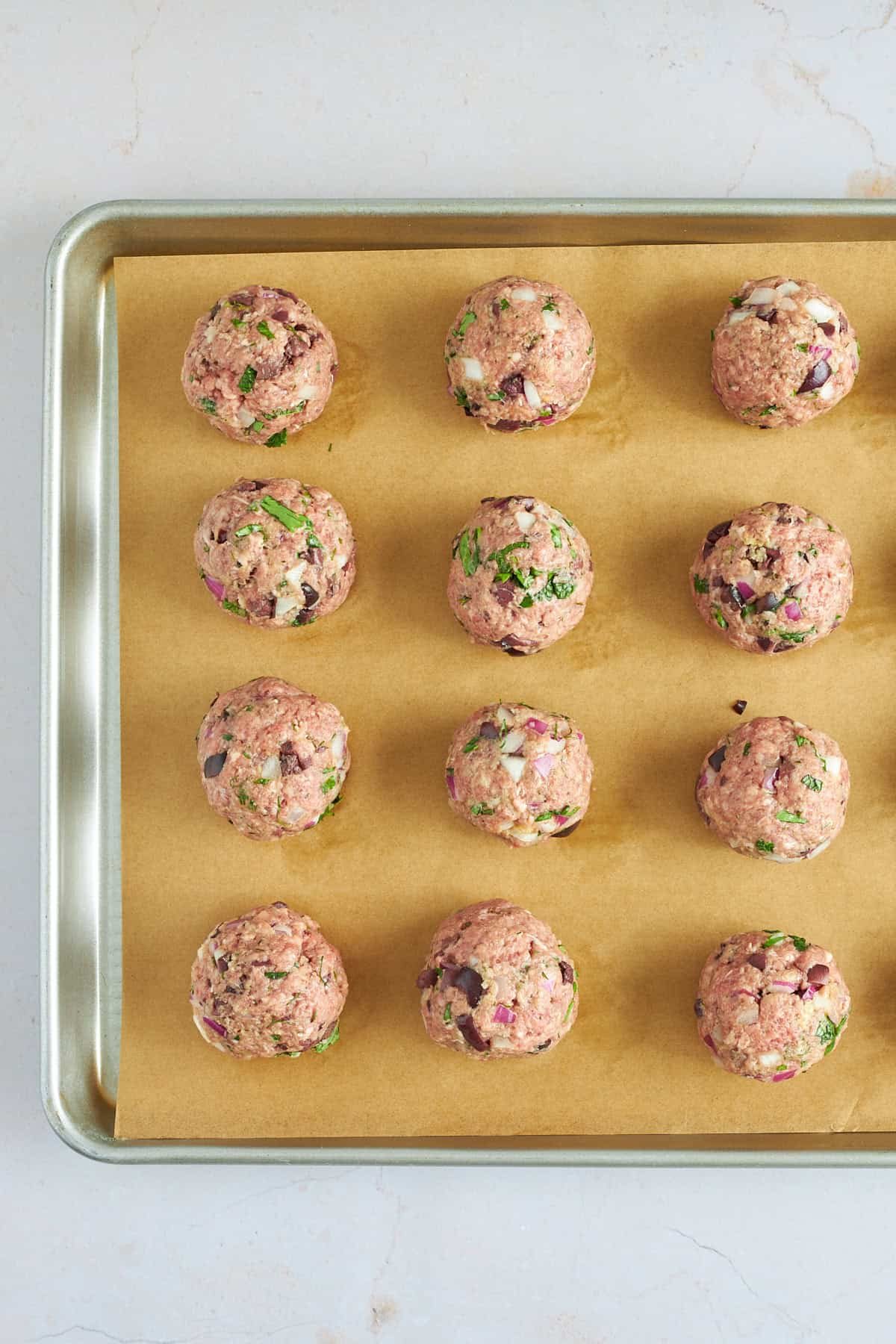 Raw beef meatballs on a baking sheet lined with parchment paper.