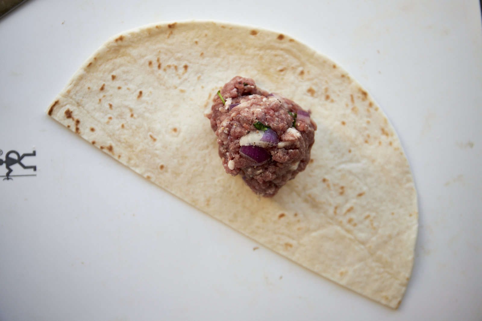 Raw ground beef in the center of a tortilla half.