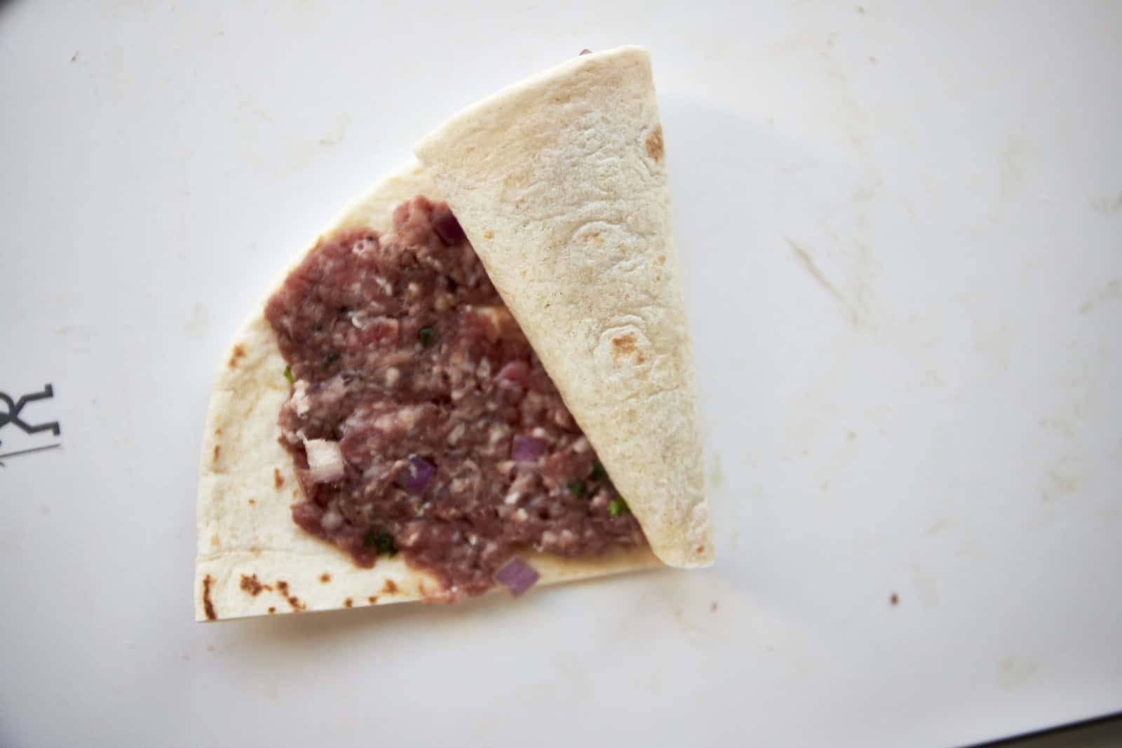 A tortilla being rolled up with ground beef in the center.