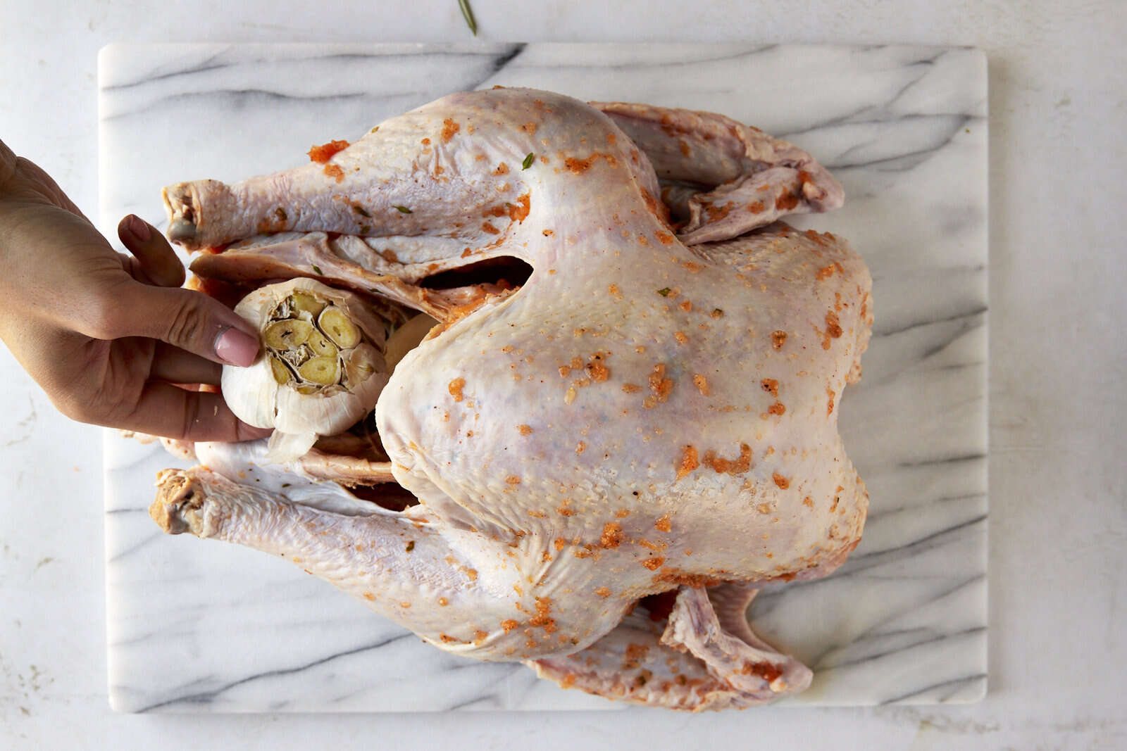 A garlic head being placed in a turkey cavity.