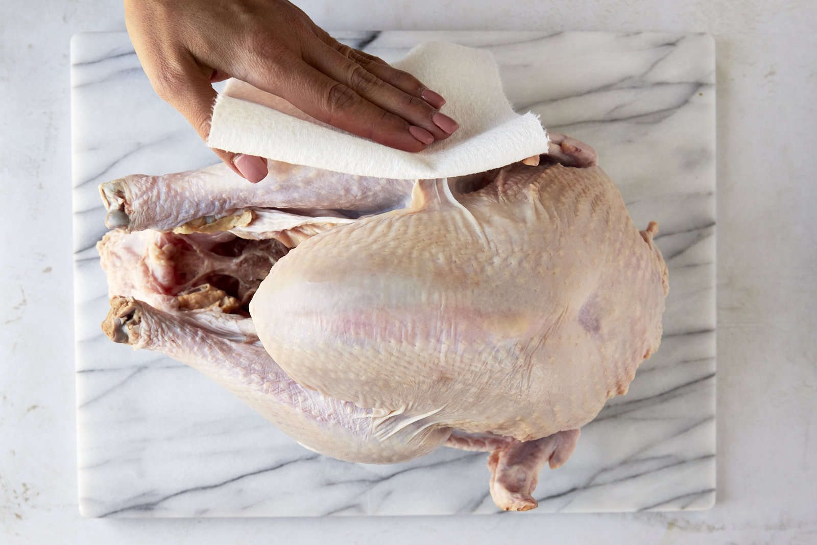 A raw turkey being pat dry.