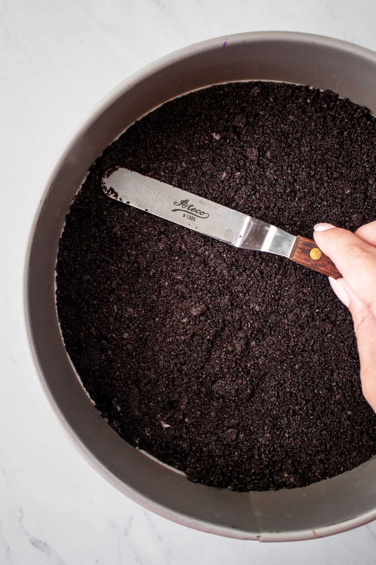 oreo crust being smoothed in the bottom of a pie tin