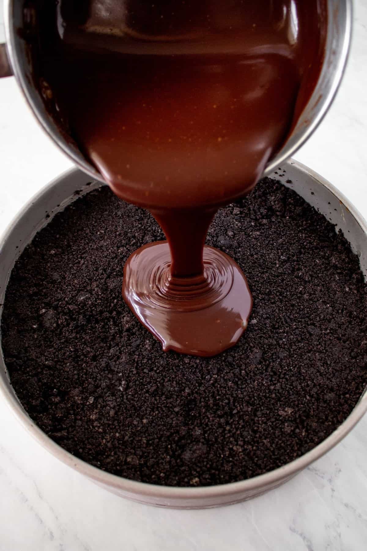 chocolate fudge being poured over a layer of chocolate crust