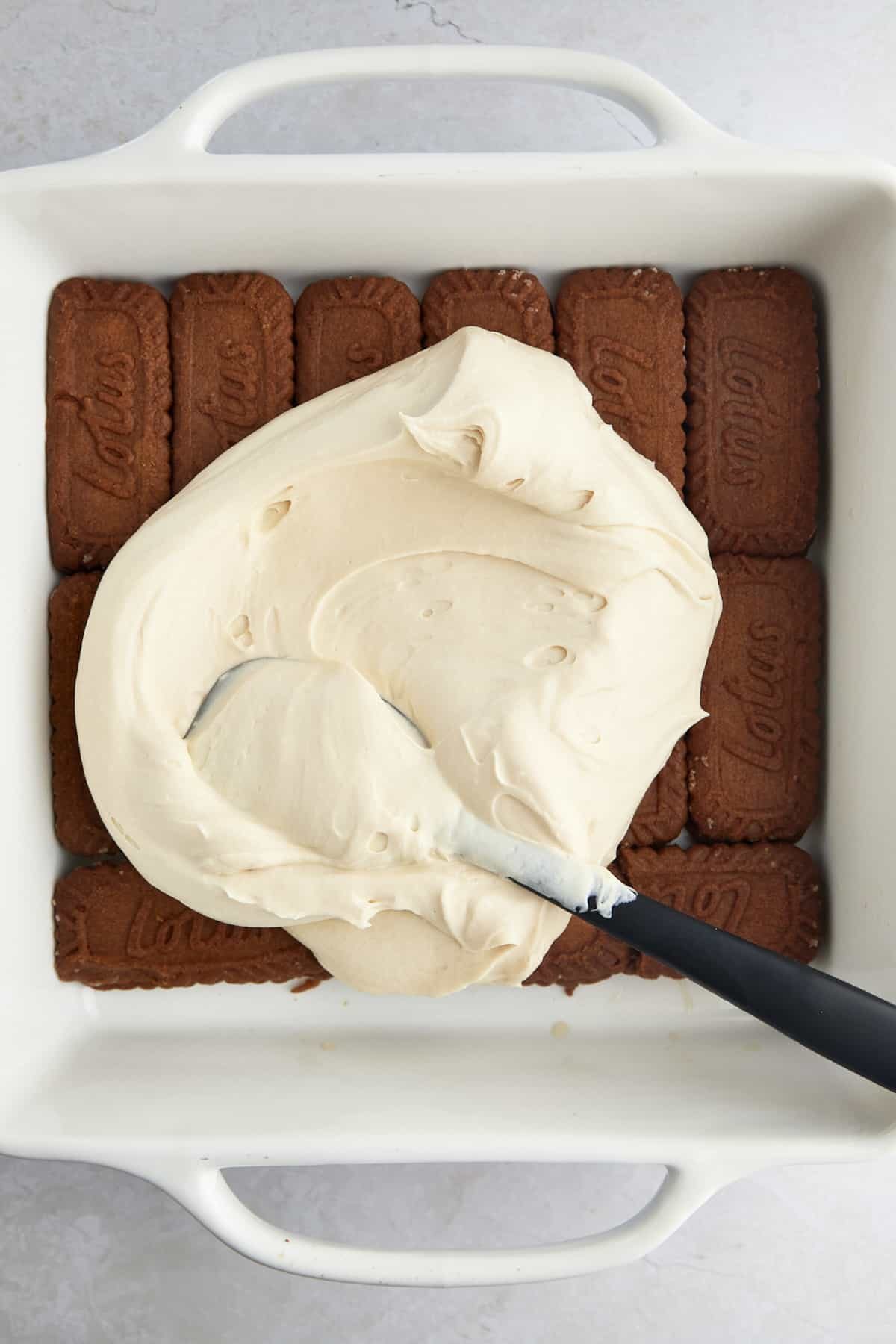 Whipped tiramisu filling being spread over espresso-soaked Biscoff cookies.