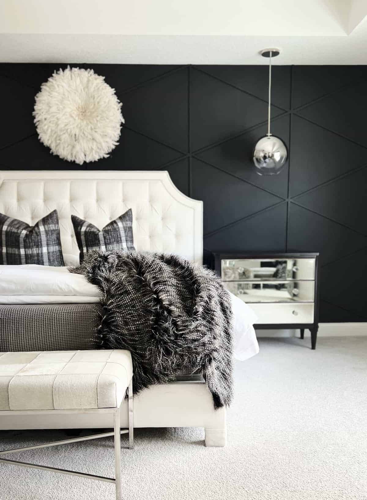 A black accent wall with wood plank diamonds in a bedroom.